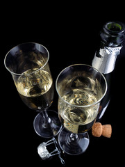 Two champagne flutes and a bottle on a black glossy background.