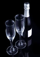 Two champagne flutes and a bottle on a black glossy background.