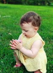 Beautiful baby girl holding flower and looking sitting on green