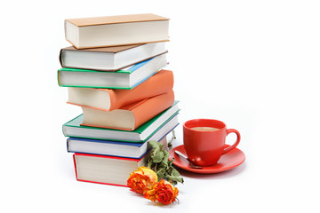 A stack of books and a cup of coffee in a saucer on a white back