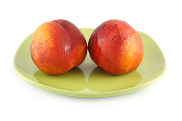 Two fresh peach on a green plate isolated on white