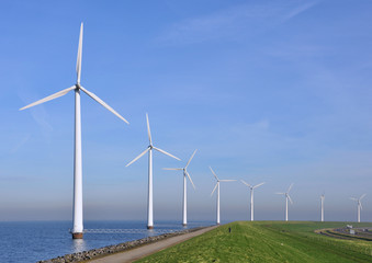 Modern windmills near the shore along a green grassy dike
