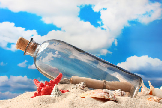 Glass bottle with note inside on sand, on blue sky background
