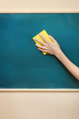 hand with a yellow sponge cleaning the chalkboard © Africa Studio