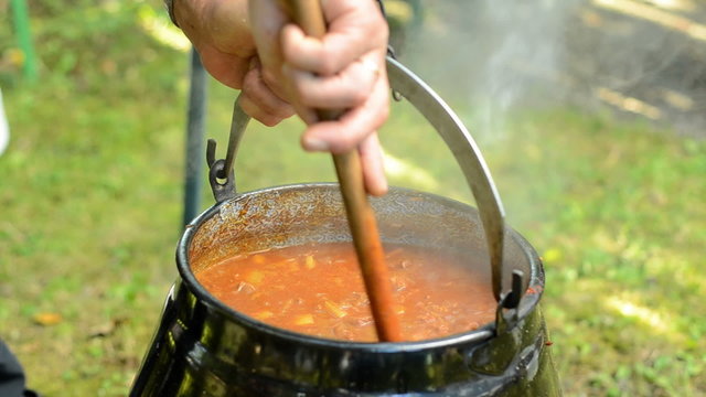 man stire one&acute;s goulash of a campfire
