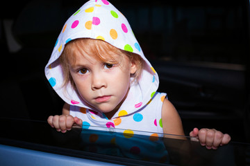 sad little girl sitting near the window in the car