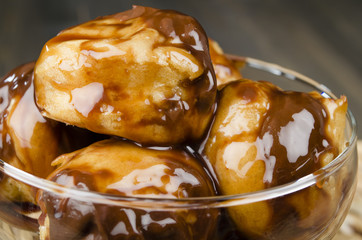 Profiteroles with chocolate sauce and syrup in a glass bowl.