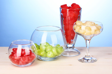 Color candies in glasses on wooden table on blue background