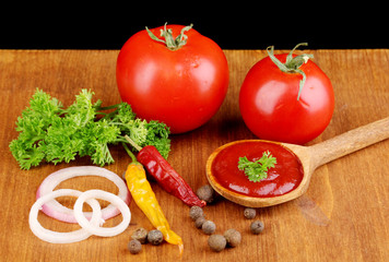 Ketchup and ripe tomatoes on wooden table on black background