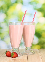 Strawberry milk shakes on wooden table on bright background