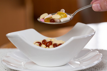 Spoon of vitamins over bowl of tablets