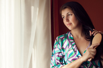 young woman at window brushes hair