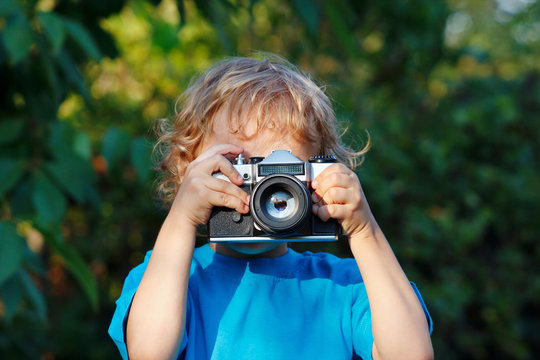 Little blond boy with a camera shoots you outdoors