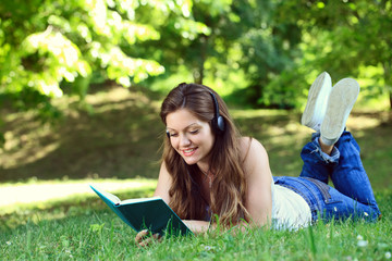 young woman with headset reading book in park