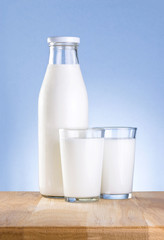Full Bottle of fresh milk and two glass is wooden table on a blu