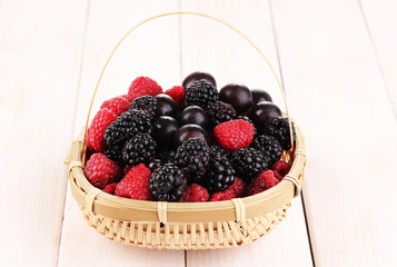 Ripe raspberries and brambles in basket on wooden table