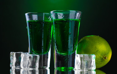 Two glasses of absinthe, lime and ice on green background