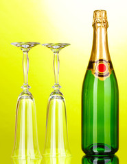 Bottle of champagne and goblets on green background