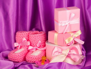 pink baby boots, pacifier, gifts on silk background.