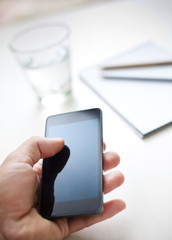 Man using smartphone, cup of water and notebook on the backgroun