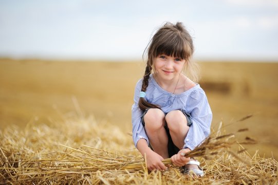 Little girl sitting on a top of haystack