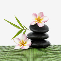 Spa stones and frangipani and a bamboo leaf on green mat