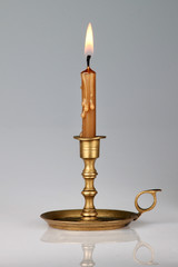 Lighted candle in an old brass candlestick, with a gray backgrou