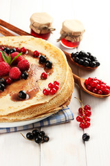Delicious pancakes with berries and jam on plate on wooden