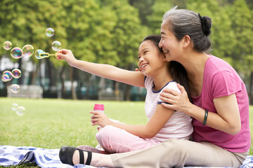 Chinese Grandmother With Granddaughter In Park Blowing Bubbles