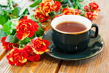 Obraz na płótnie Canvas cup of tea and roses bouquet on wooden table