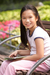 Chinese Girl Sitting On Park Bench With Digital Tablet