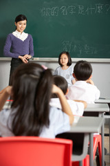 Pupil And Teacher Standing By Blackboard In Chinese Classroom