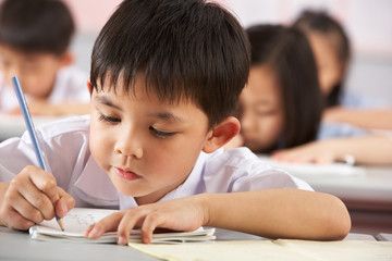 Group Of Students Working At Desks In Chinese School Classroom