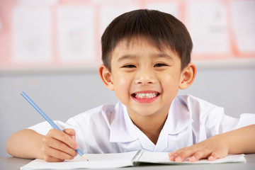 Male Student Working At Desk In Chinese School Classroom