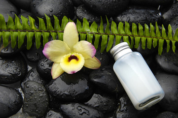 massage oil with fern and yellow orchid on black pebble