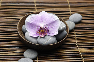Pink orchid and stones in bowl on bamboo mat
