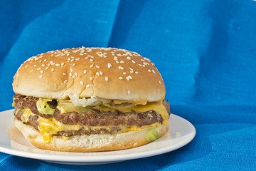 Cheeseburger lying on a white plate with blue linen background