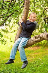Счастливый мальчик сидит на ветке дерева и смеётся