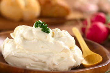 Fresh cream cheese spread on wooden plate with chives