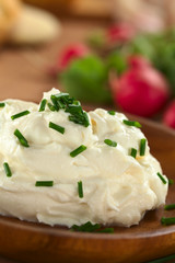Fresh cream cheese spread on wooden plate with chives