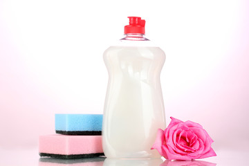 Dishwashing liquid with sponges and flower on pink background