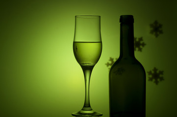 bottle and glass with white wine on green background