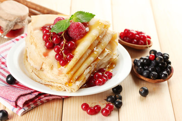 Delicious pancakes with berries, jam and honey on wooden table