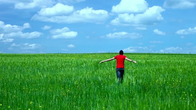 Boy running in a field of green wheat