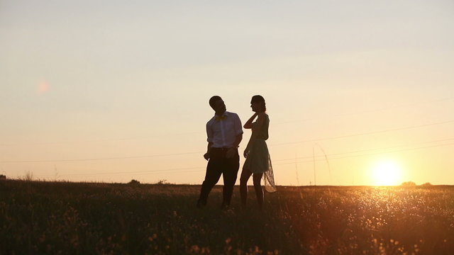 Young couple silhouettes dancing on the field at sunset
