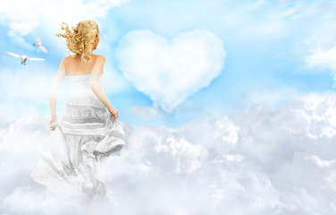 Happy young woman running across clouds in the sky. Heart on bac