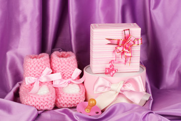 pink baby boots, pacifier, gifts on silk background.