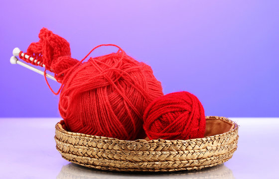 Red knittings yarns in basket on purple background