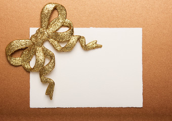 Fototapeta na wymiar Blank gift tag tied with a gold bow on gold paper