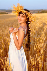 Young woman with chaplet in white dress standing in field